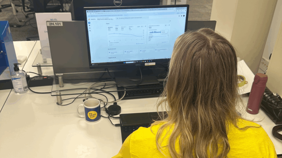 Person wearing yellow t-shirt sitting at a desk looking at data on a screen, with their back to the camera.