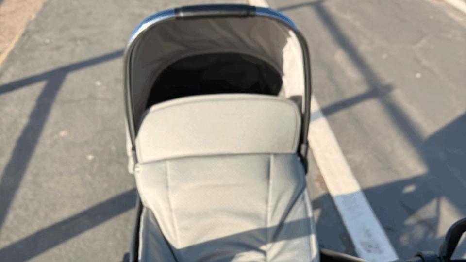 A grey buggy getting pushed along on a sunny day.