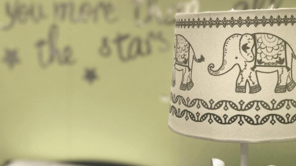 A lampshade in a child's bedroom with picture of elephants on it.