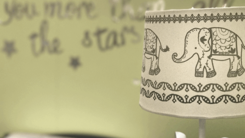 A lampshade in a child's bedroom with picture of elephants on it.