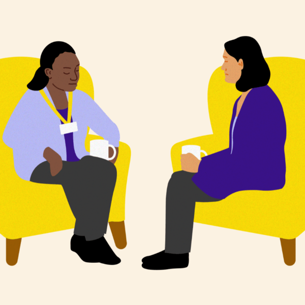 Two people sitting on yellow armchairs facing each other. One person has a mug in their hand.