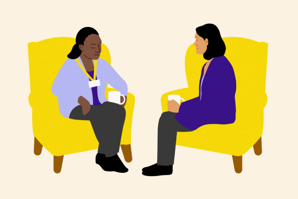 Two people sitting on yellow armchairs facing each other. One person has a mug in their hand.