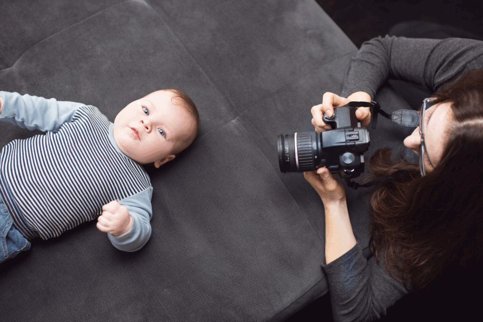A baby lying on their back while a photographer kneels down beside them and takes a photo.