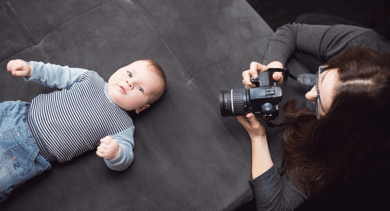 A baby lying on their back while a photographer kneels down beside them and takes a photo.