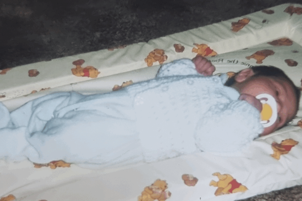 Baby Nerice lying on her back, asleep in a blue babygrow.