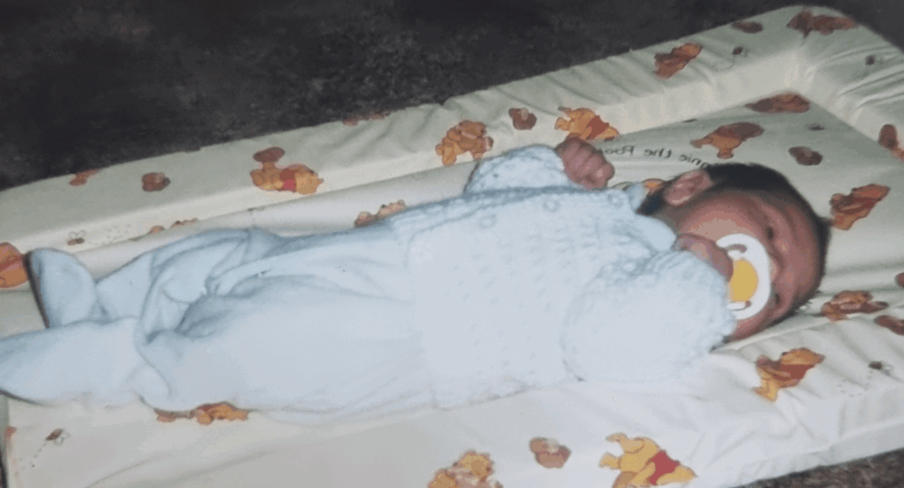 Baby Nerice lying on her back, asleep in a blue babygrow.