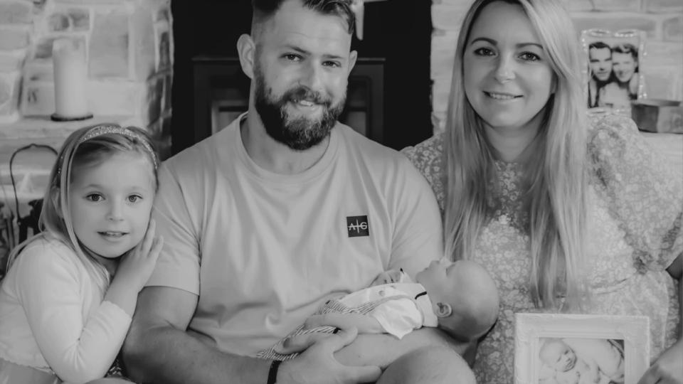 Katie and her family smiling at the camera in a black and white picture. There is Katie, her husband Christian, and their children Ellis and Theia.