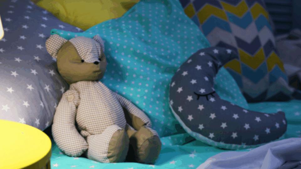 A teddy bear and a moon-shaped toy, on a bed.
