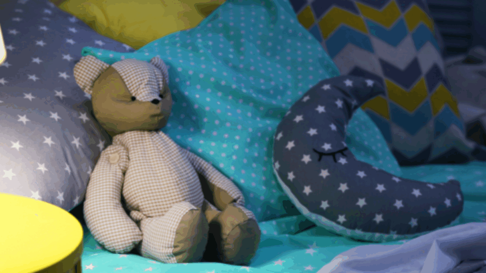 A teddy bear and a moon-shaped toy, on a bed.