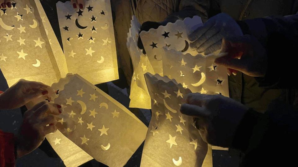 People holding lit up lanterns with cut outs of moons and stars in them, at nighttime.
