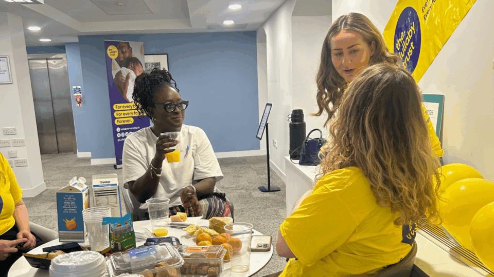 Seyi at The Lullaby Trust offices, chatting to staff whilst enjoying the snacks laid out.