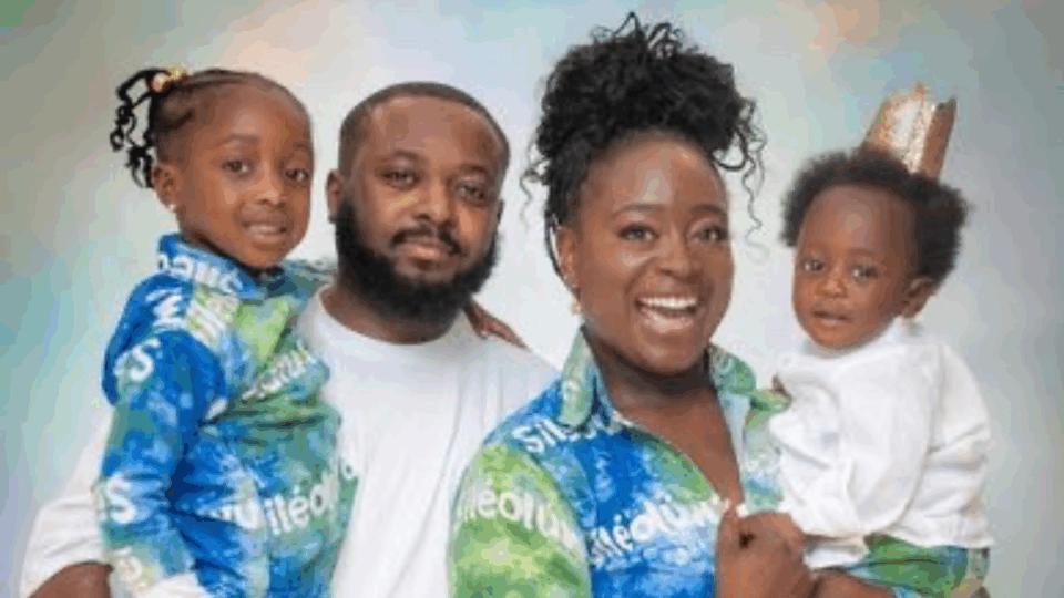 Seyi with her partner and two children, wearing blue and green matching clothes, all smiling at the camera.
