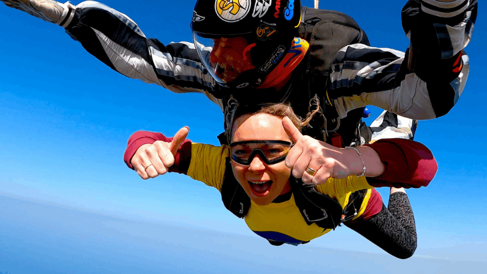 Katie strapped to an instructor, in the middle of her skydive giving thumbs up to the camera.