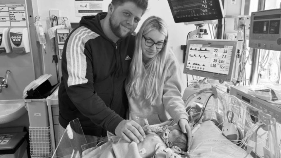 Hayley and Dimitri standing by the bed that Violet is sleeping in.