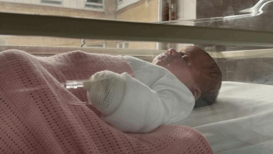 Baby Violet lying in a cot on her back with a pink blanket.