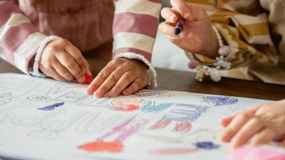 Kids drawing and colouring in, it is a close up of their hands and their art.