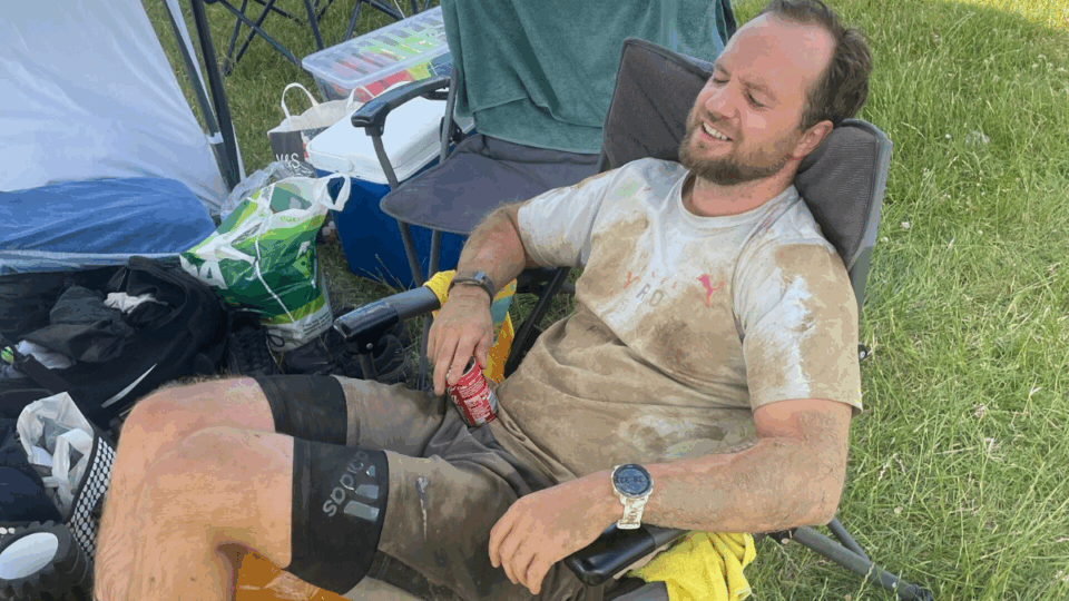 Stefan sitting in a chair looking tired, wearing a very muddy t-shirt.