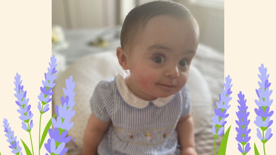 Gigi is looking around the camera to who is taking the photo, wearing a blue striped romper suit. She is sat on an adult bed.