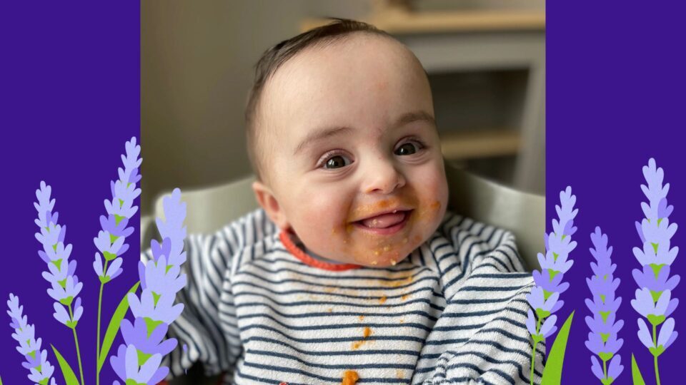 Gigi is smiling brightly in her highchair. She has spaghetti Bolognese around her mouth.