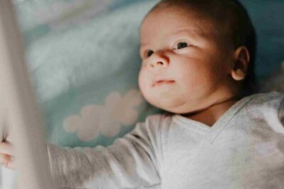 Baby lying on their back, looking out through the slats of the cot.