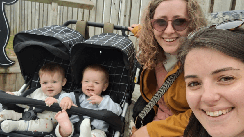 Izzy and Laura taking a selfie smiling at the camera, next to twins Alo and Jovie in a pram.