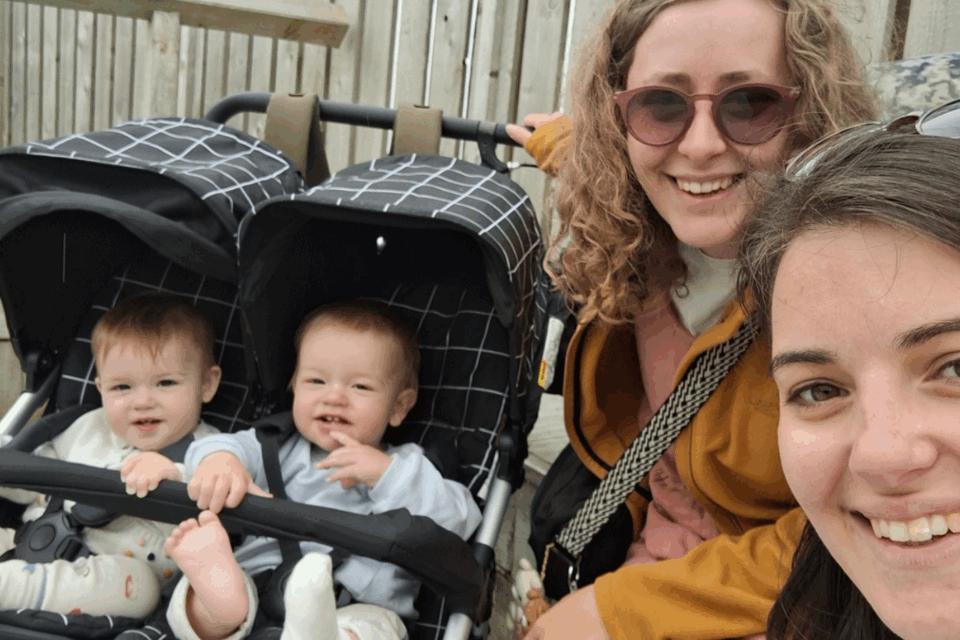 Izzy and Laura taking a selfie smiling at the camera, next to twins Alo and Jovie in a pram.