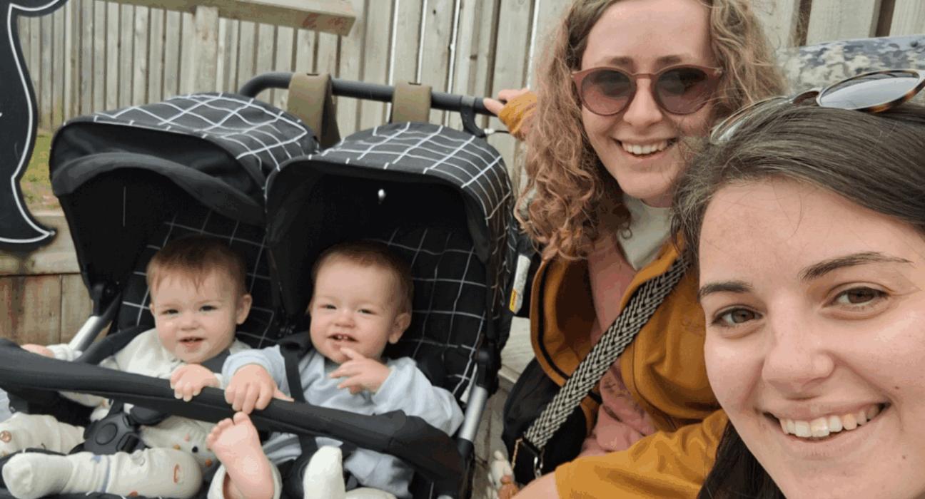 Izzy and Laura taking a selfie smiling at the camera, next to twins Alo and Jovie in a pram.