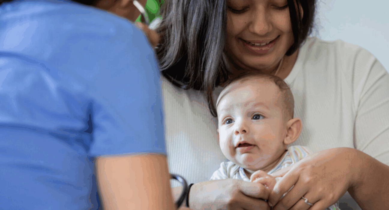 Lady holding her baby. There is also a health professional with their back to us.