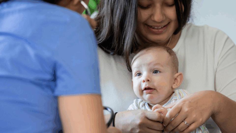 Lady holding her baby. There is also a health professional with their back to us.