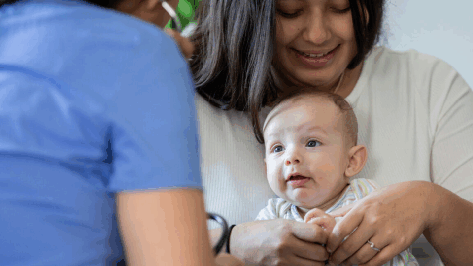 Lady holding her baby. There is also a health professional with their back to us.