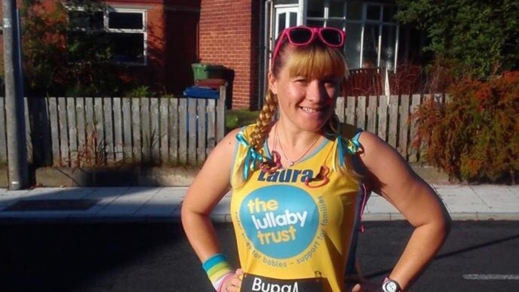 Laura wearing a Lullaby Trust running vest, smiling at the camera with her hands on her hips. She has pink sunglasses on her head and bows in her hair.