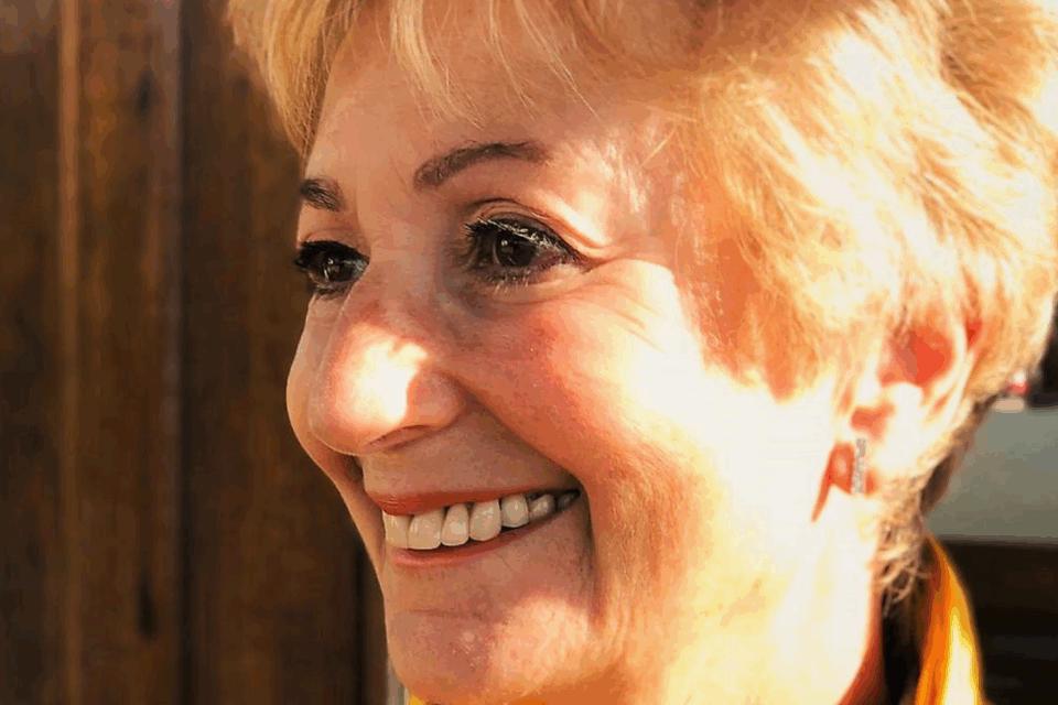 Close up of Judi, with blond hair, smiling away from the camera.