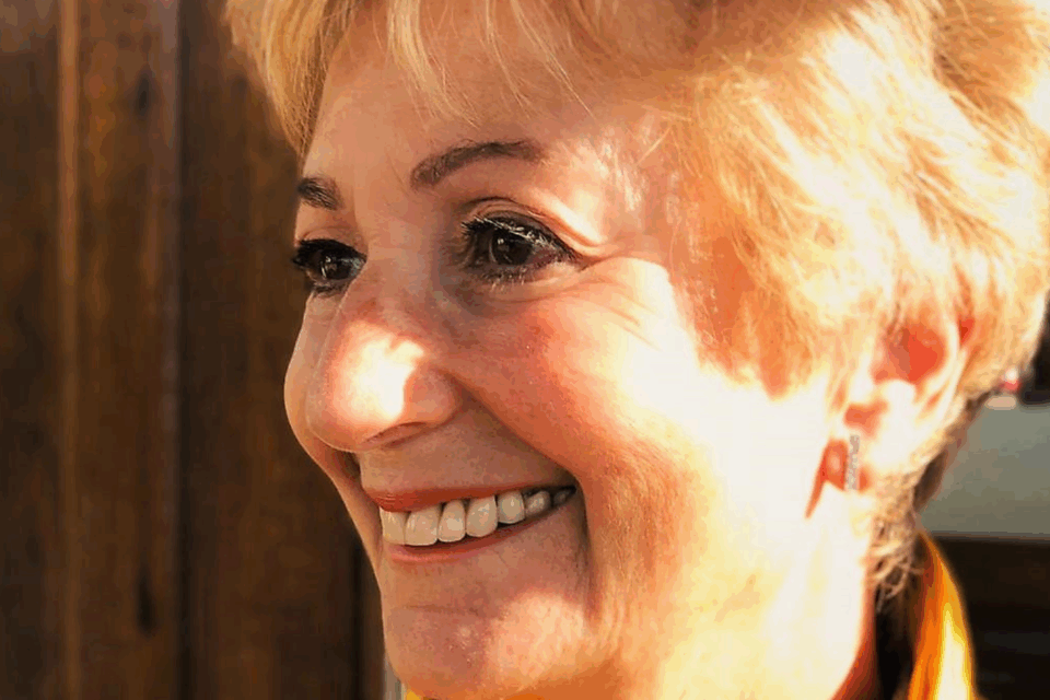Close up of Judi, with blond hair, smiling away from the camera.