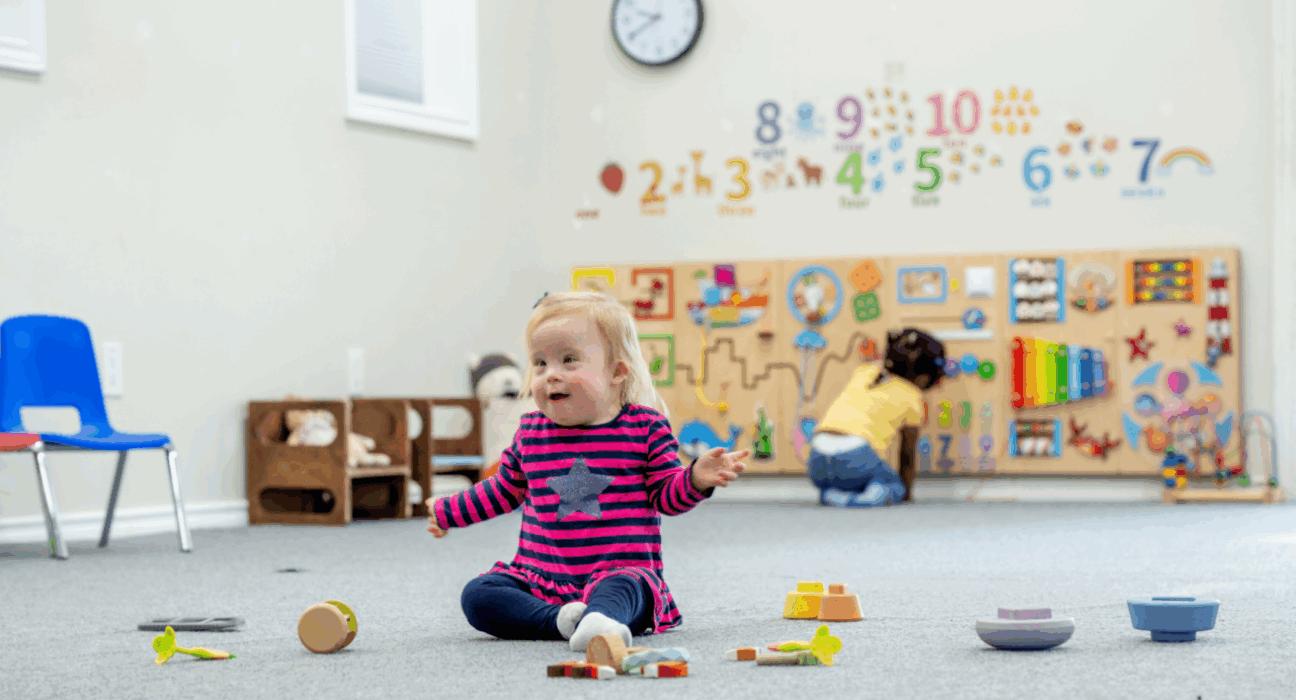 Child playing in nursery with toys scattered on the floor.