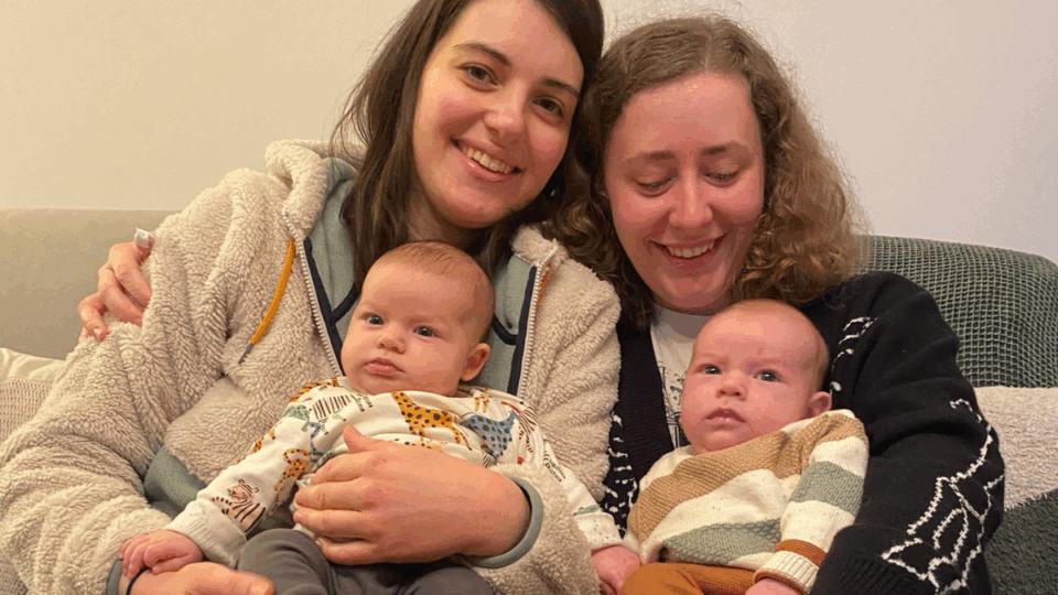 Izzy and Laura sitting next to each other on the sofa, holding Alo and Jovie.