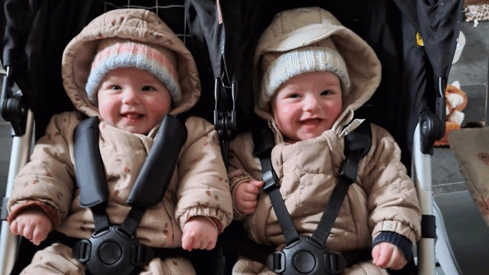 Alo and Jovie sitting beside each other in a twin pram.
