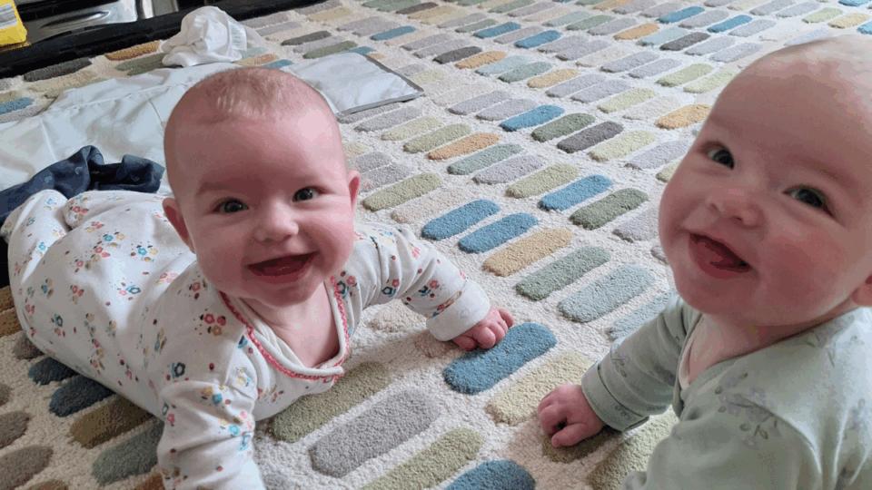 Alo and Jovie having tummy time on the floor. They are both looking up at the camera smiling.