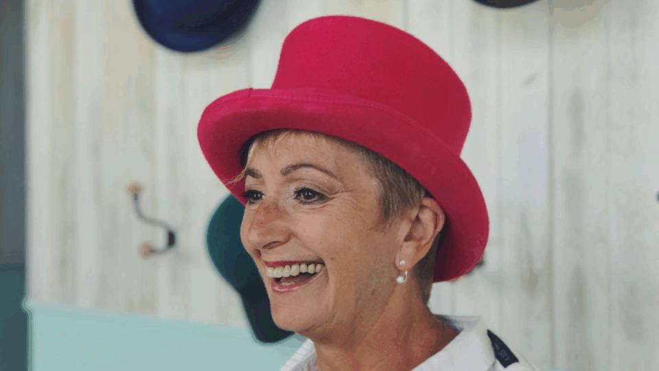 Judi smiling away from the camera, wearing a red hat.