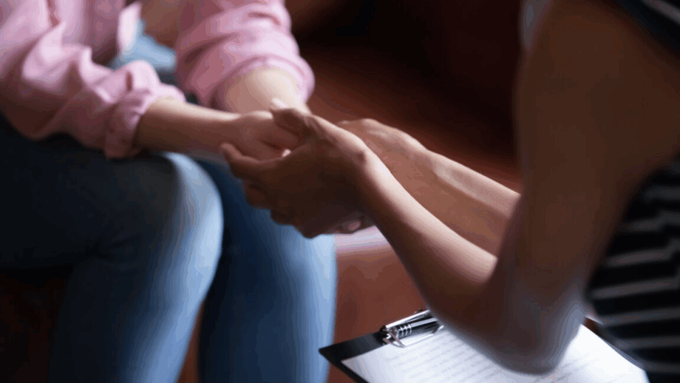 Close up of people holding hands whilst sitting facing each other.