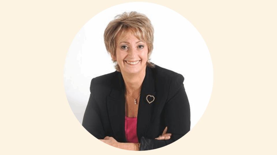 Judi wearing a blazer and a pink top, with her arms crossed smiling at the camera.