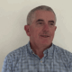 Dr Edward Doyle wearing a blue and white shirt, standing in front of a white background, looking just beyond the camera.