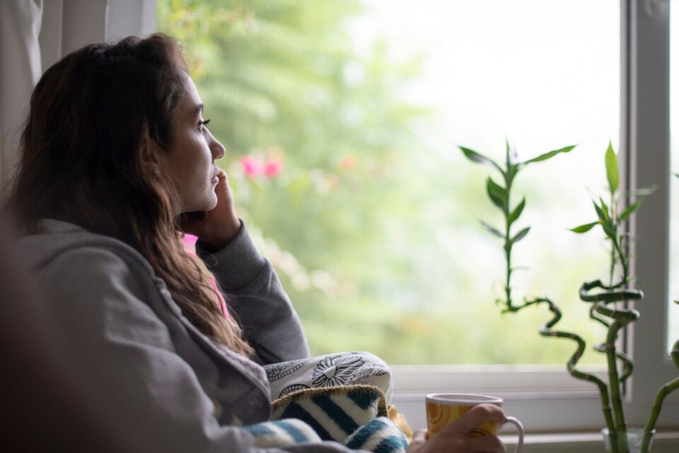 A woman is resting her chin on her hand, looking out of the window. Her side profile looks sad.