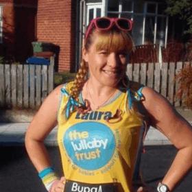 Laura wearing a Lullaby Trust running vest, smiling at the camera with her hands on her hips. She has pink sunglasses on her head and bows in her hair.