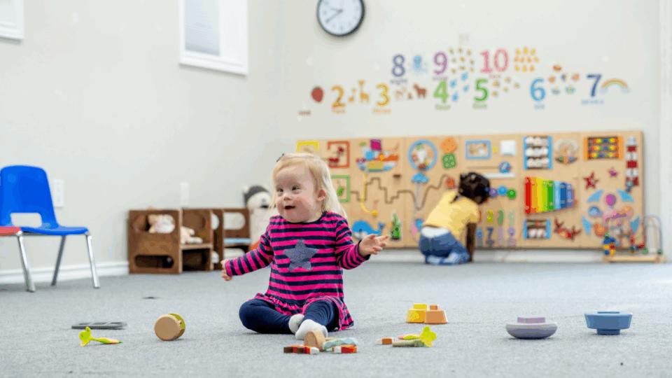 Child playing in nursery with toys scattered on the floor.