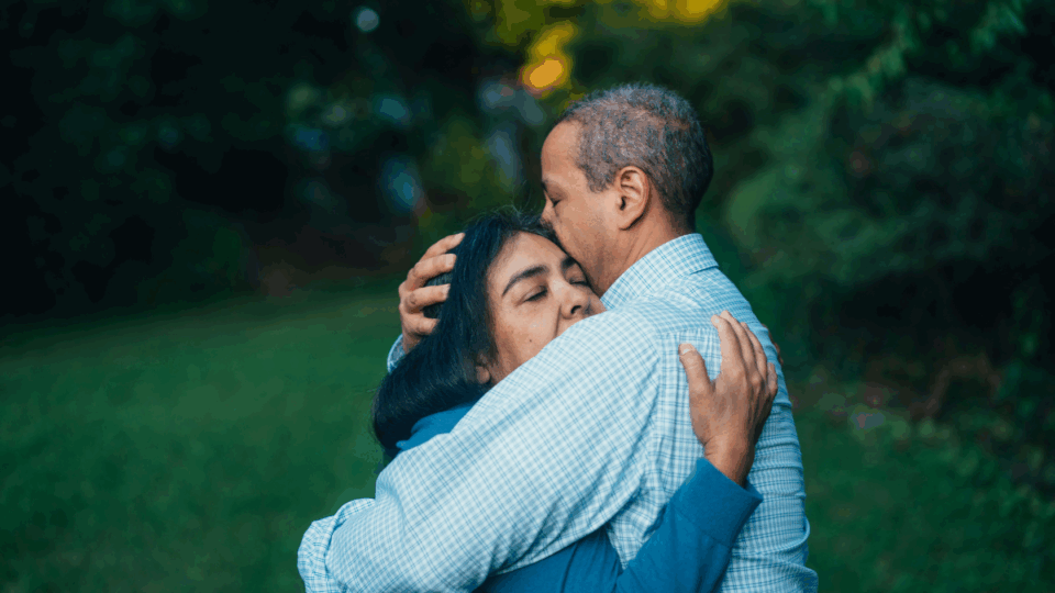A man and a woman standing outside, hugging.