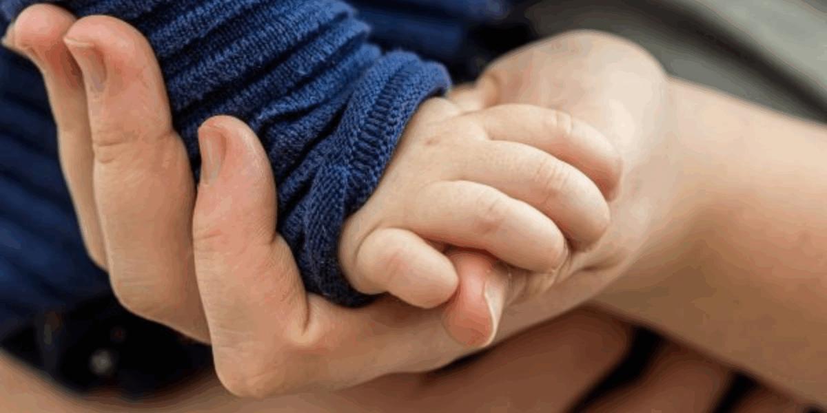 Baby's hand on an adult's hand, close up.