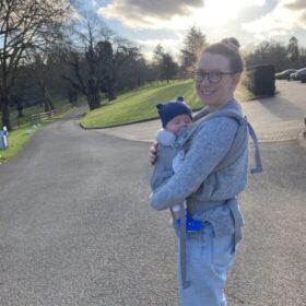 Laura standing outside holding her little one.