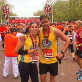 Two runners in yellow lullaby trust vests smiling after a race with medals around their necks