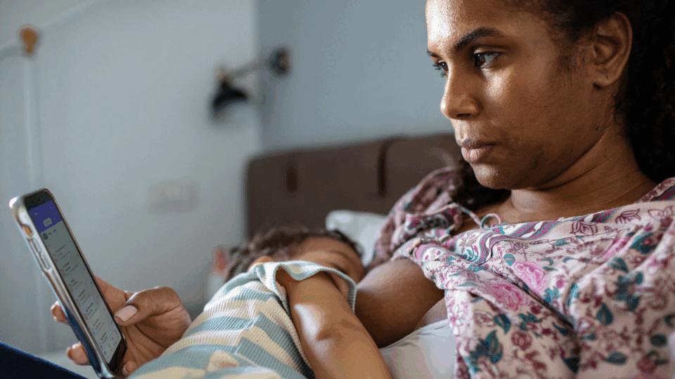 Close up of a Young mother using a phone whilst breastfeeding her young baby son