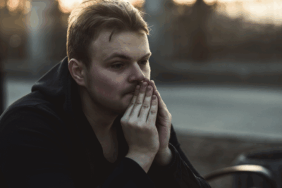 A man is looking into the distance with his hands up to his mouth. He looks deep in thought, and quite sad. The sun is setting behind him.